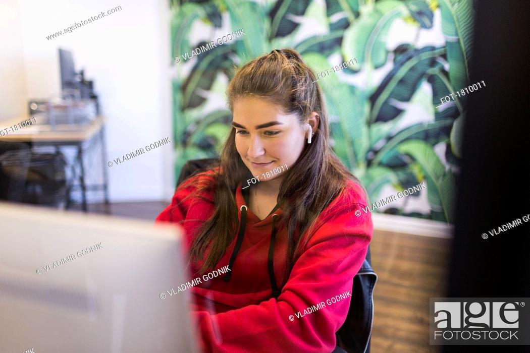 Stock Photo: Young woman with wireless earbuds using computer in internet cafe.