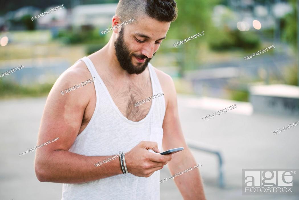 Imagen: Young man with shaved head looking at cell phone.