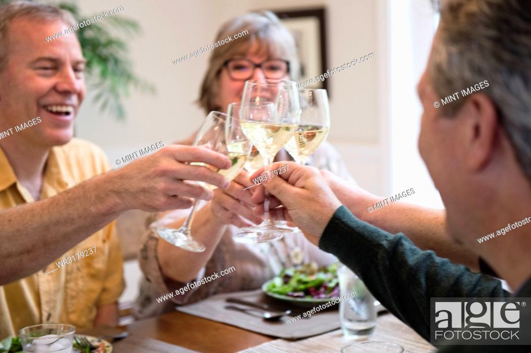 Stock Photo: Senior couples toasting a home dinner party with glasses of white wine.