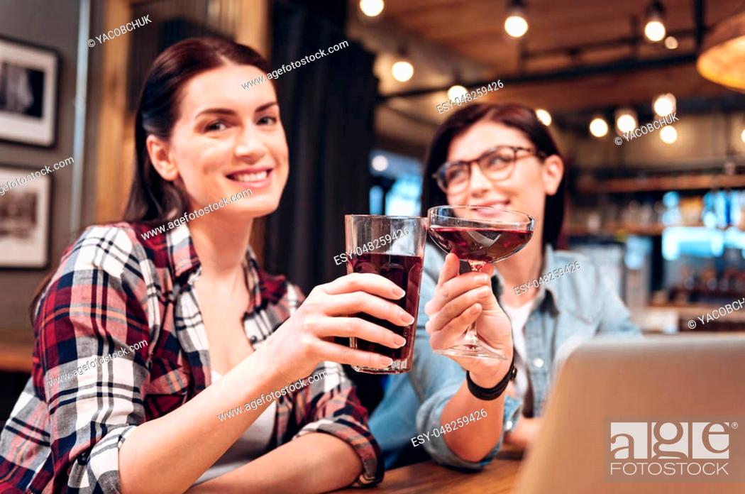 Stock Photo: Just smile. Happy smiling girl keeping glass with juice in right hand sitting near her friend while looking straight at camera.