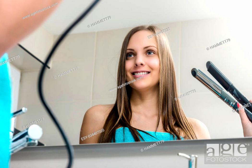 Stock Photo: Smiling woman curling hair with straightener.