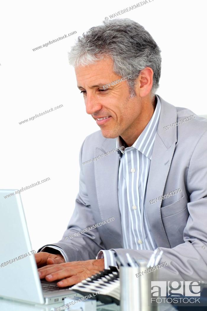 Stock Photo: Smiling confident businessman working at a computer at his desk.