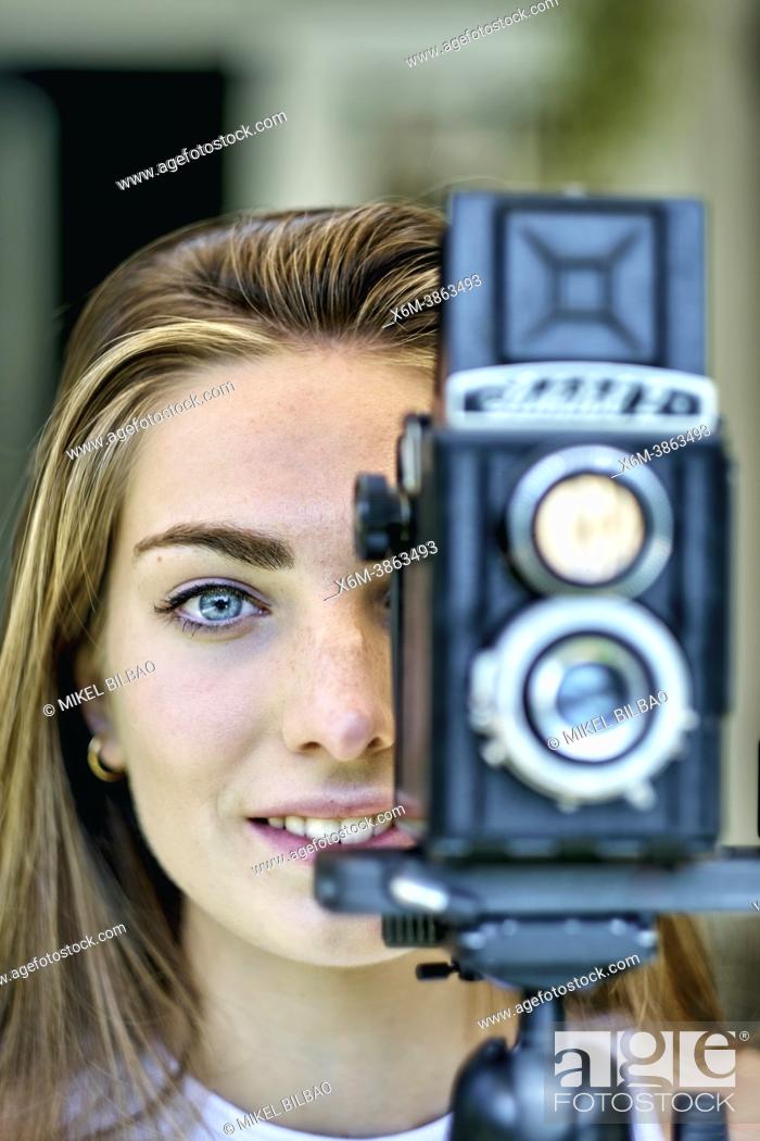 Stock Photo: Portrait of a young beautiful caucasian woman in her 20's with blue eyes photographing with an old vintage camera on a tripod outdoor.