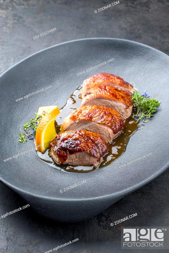 Stock Photo: Traditional roasted Christmas duck breast with orange slice and herbs as closeup on a modern design plate.
