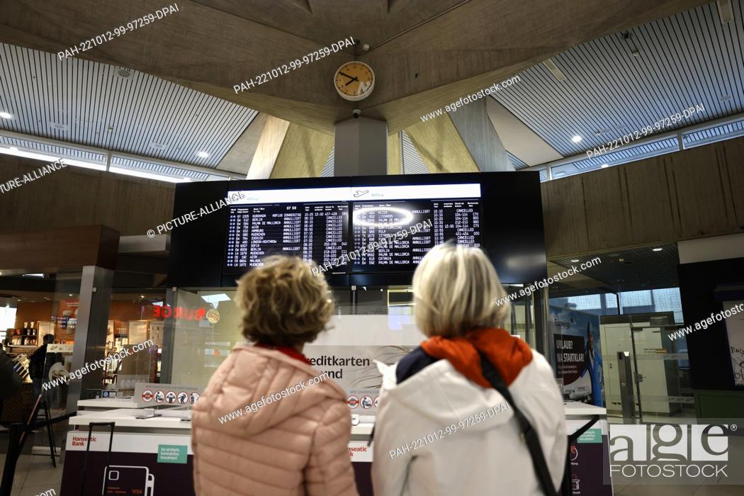 Stock Photo: 06 October 2022, North Rhine-Westphalia, Cologne: Two travelers stand in front of a display showing the cancelled flights.