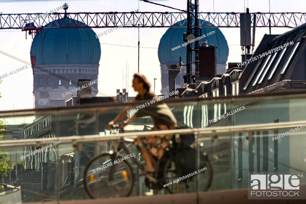 Stock Photo: 13 June 2021, Bavaria, Munich: A woman is cycling across a bridge that spans Landsberger Strasse. The two towers of the Frauenkirche tower in the background.