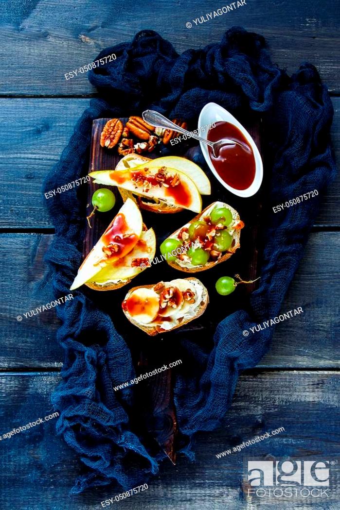 Stock Photo: Healthy crostini with pear, cream-cheese, grapes, banana, nuts and chocolate caramel. Top view of breakfast toasts or snack sandwiches on vintage chopping board.