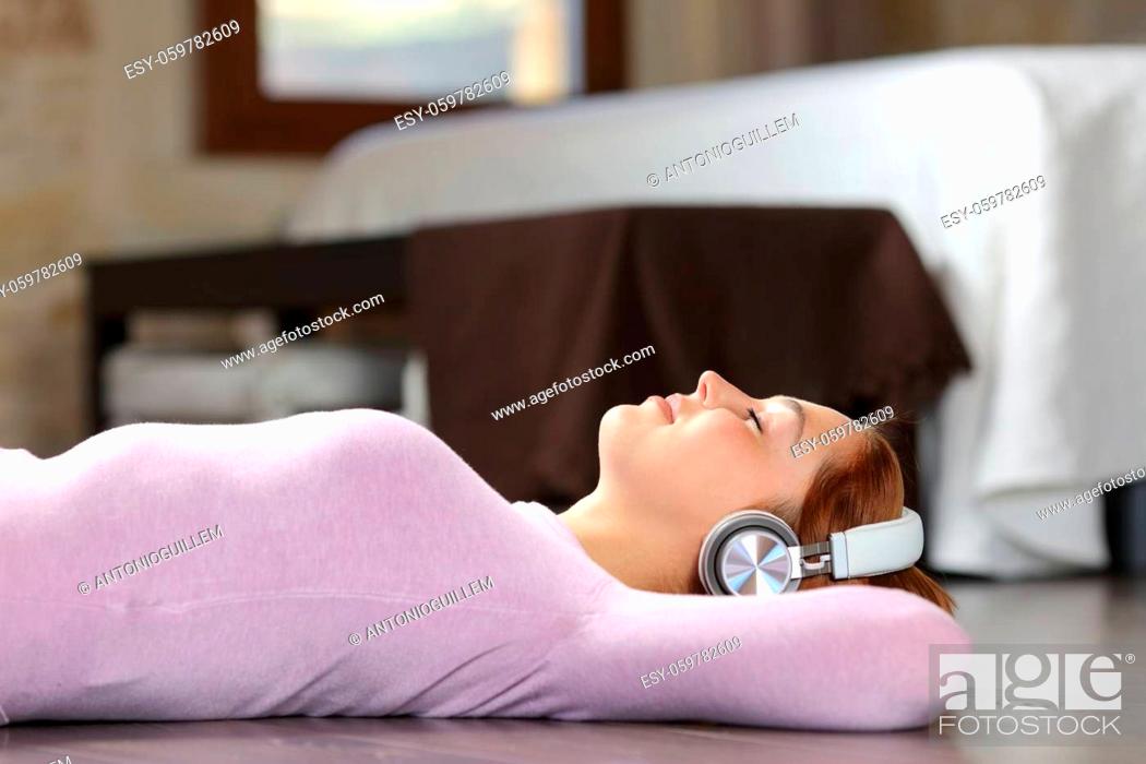 Stock Photo: Side view portrait of a woman lying on the floor listening to music with headphones in the bedroom.
