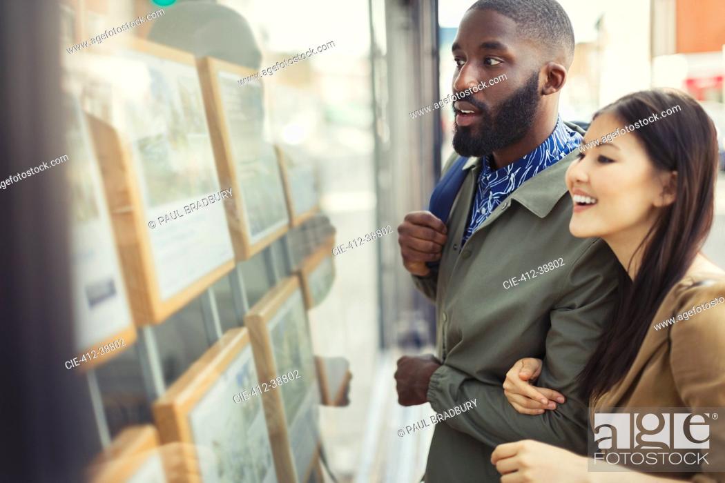Stock Photo: Young couple browsing real estate listings at storefront.