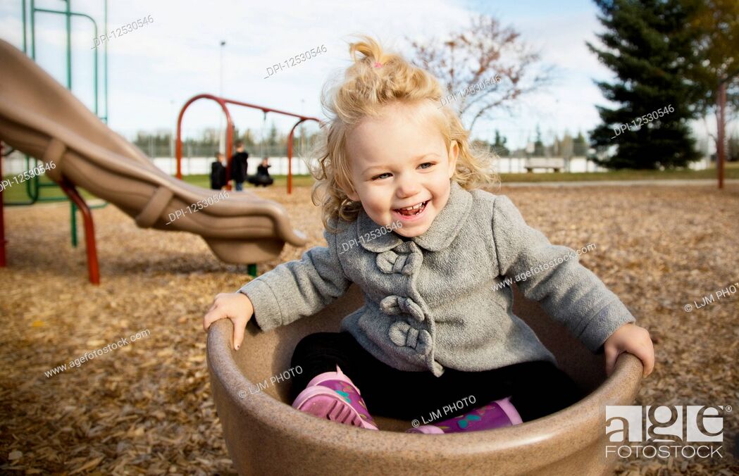 Stock Photo: A cute young girl spinning in a saucer on a playground during the fall season; Spruce Grove, Alberta, Canada.