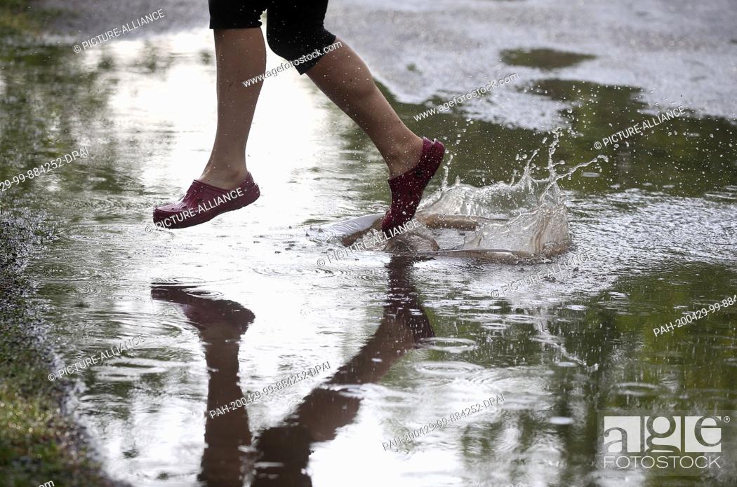 Stock Photo: 29 April 2020, Berlin: A young woman walks through large puddles of rain in the Köpenick district, which have formed on the streets after a heavy rain shower.