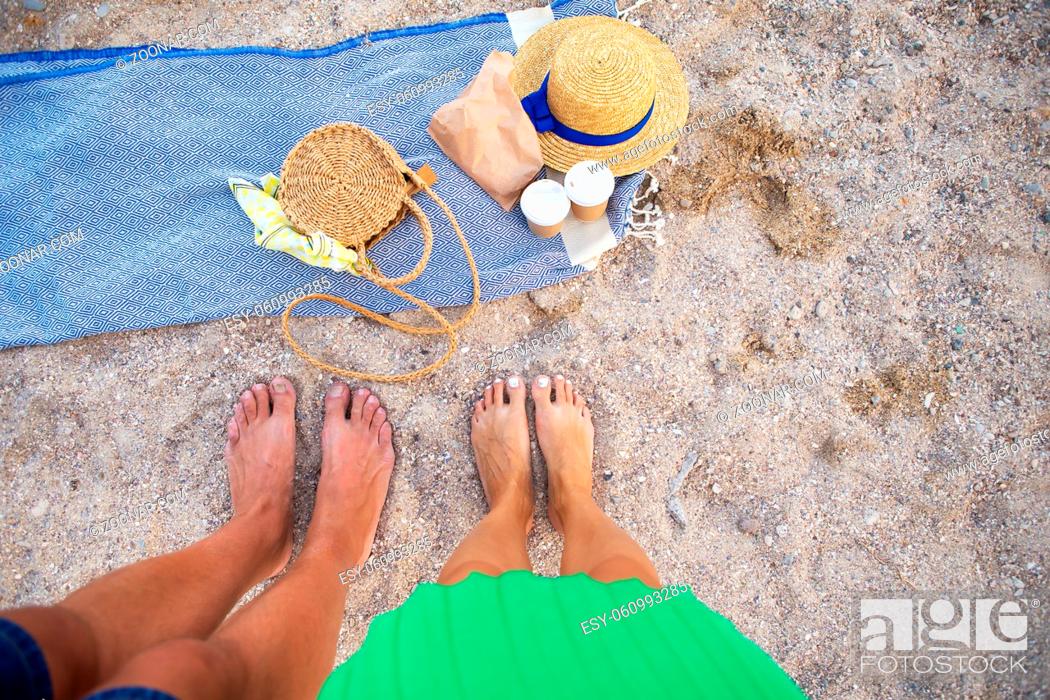 Stock Photo: Picnic near the sea. A blue plaid on which are glasses with coffee, a bag, a hat. Feet of a couple in love. View from above.