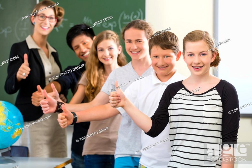 Stock Photo: School class teacher and students stand in front of a blackboard with math work in a classroom during lesson.