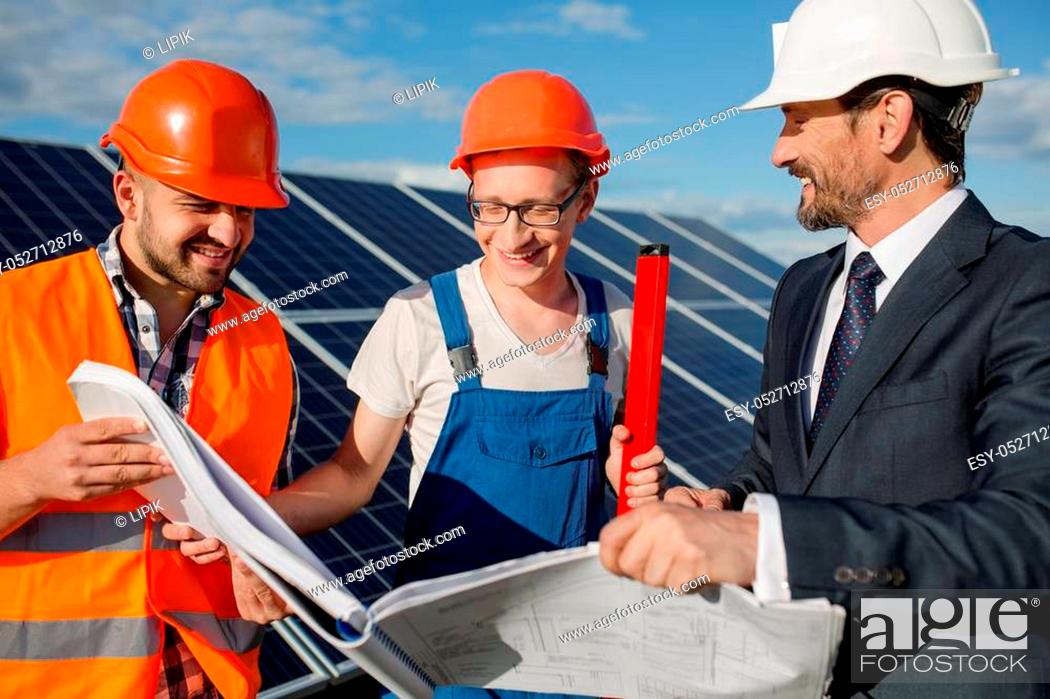 Stock Photo: Director, foreman and worker looking in technical drawings at solar energy station. Three men exploring technical documentation, solar panels on backstage.