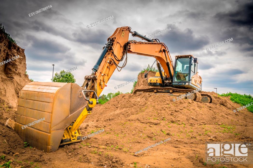 Stock Photo: a yellow excavator stands on a mound of earth on a large construction site.