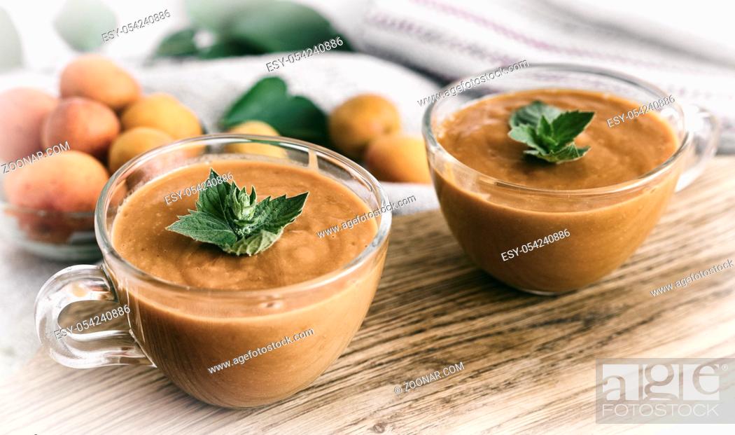 Stock Photo: Two cups apricot smoothie decorated with mint petals. There are whole apricots nearby.