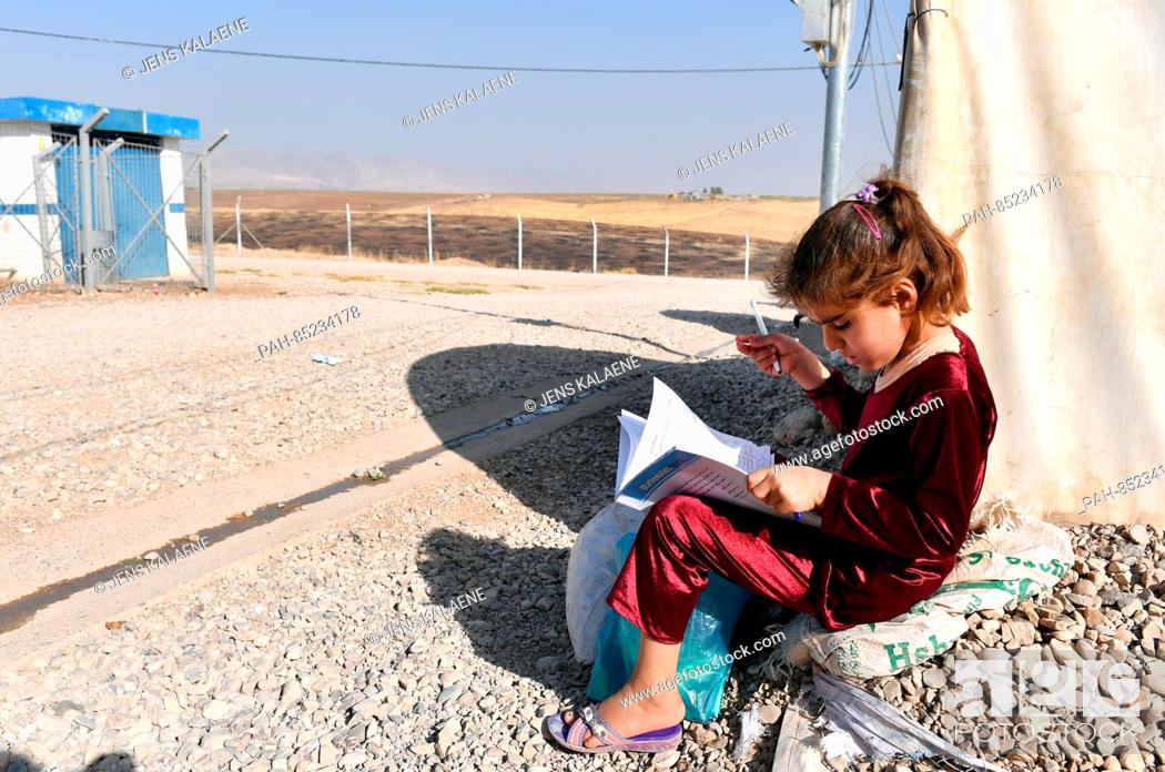 Stock Photo: A girl sits with a schoolbook for math and studies by her family's tent in the Mamilian refugee camp in the Dohuk region, Iraq, 19 October 2016.