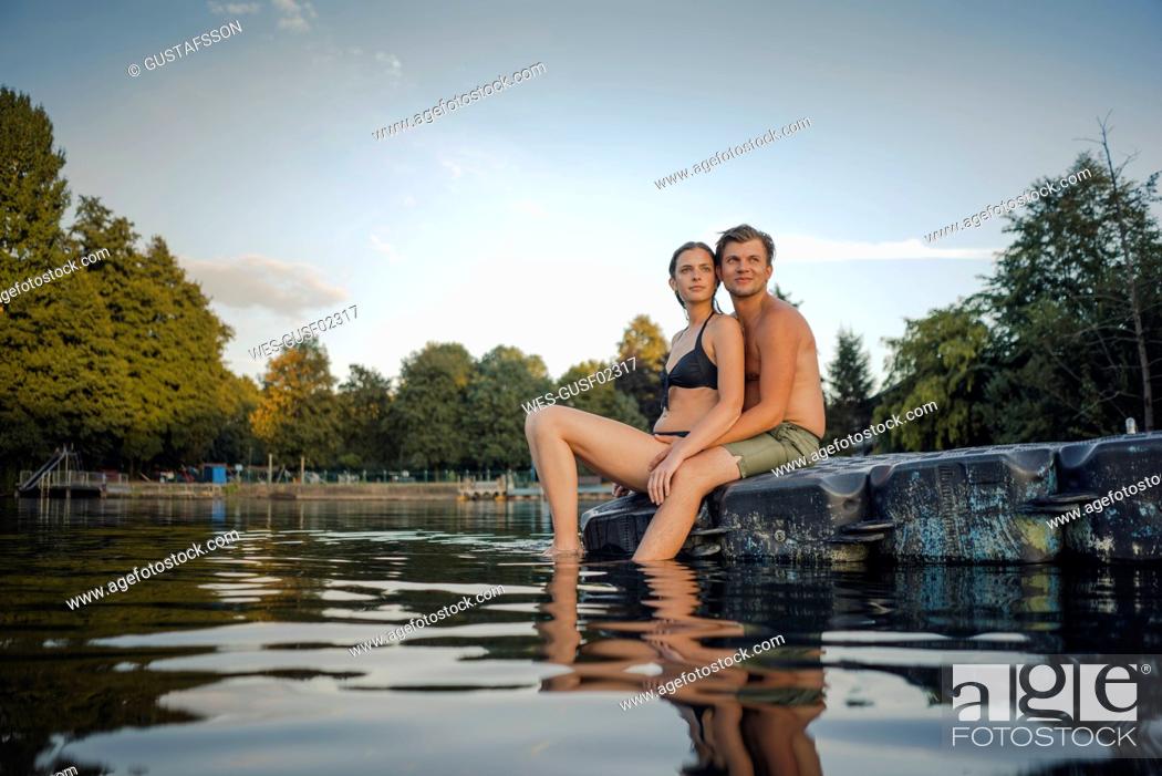 Stock Photo: Young couple sitting on bathing platform on a lake looking at distance.