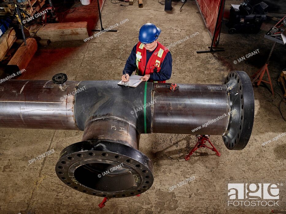 Photo de stock: A tradesman stands at a large pipe and writes on a document; Edmonton, Alberta, Canada.