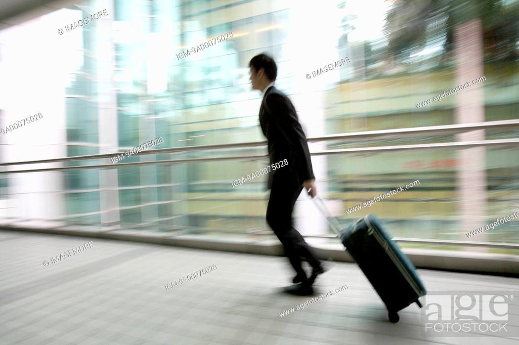 Stock Photo: Businessman running with rolling suitcase, blurred motion.