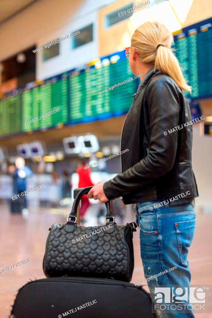 Stock Photo: Casually dressed young stylish female traveller checking a departures board at the airport terminal hall in front of check in couters.