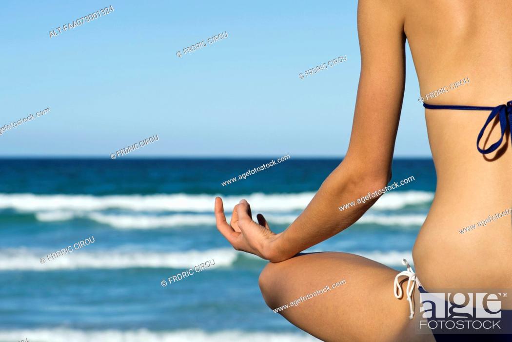 Stock Photo: Woman in bikini sitting in lotus position by sea, rear view.