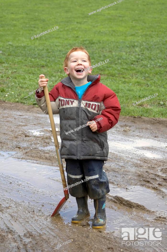 Stock Photo: Boy plays and has fun on a rainy day with a spade in the mud.