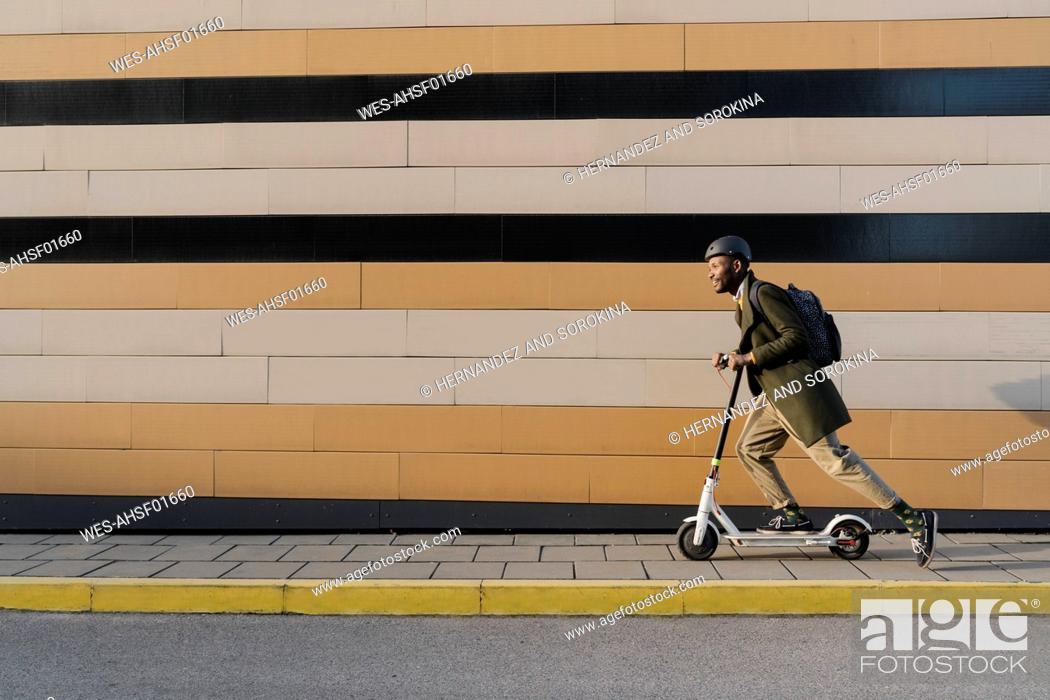 Stock Photo: Stylish man with helmet and scooter passing a building.