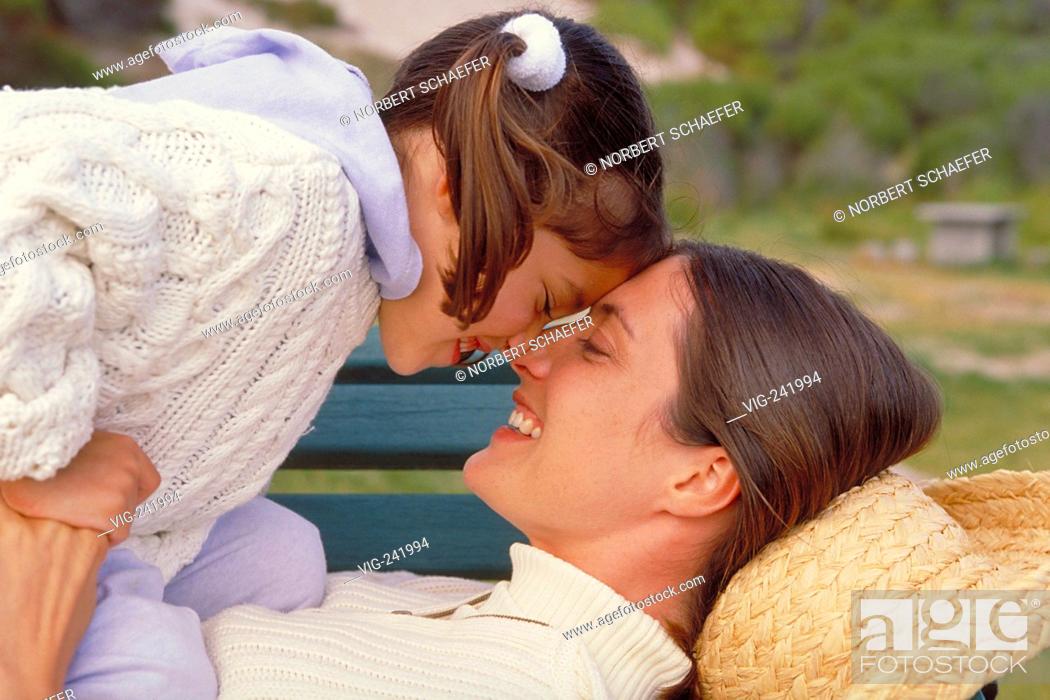 Stock Photo: portrait, outdoor, mother and her 8-year-old daughter lay down on a park bench smooching, both wearing white pullover  - GERMANY, 21/08/2004.