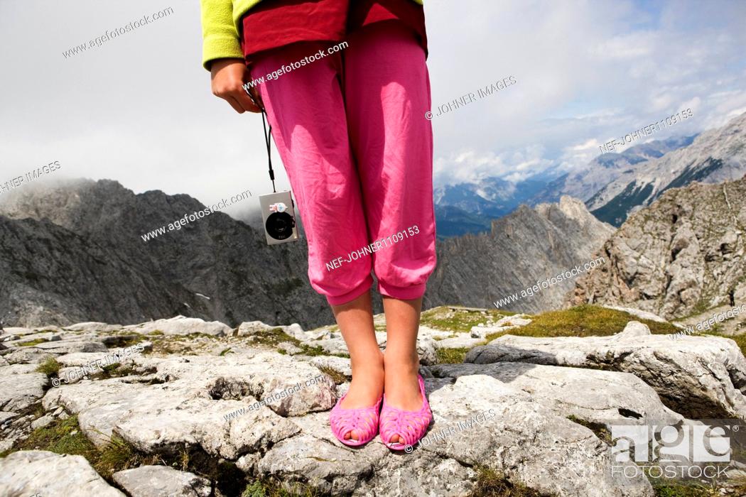 Stock Photo: Low section of tourist standing on rock and holding digital camera.
