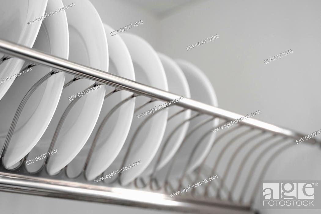 Stock Photo: Dish drying metal rack with big nice white clean plates. Traditional comfortable kitchen. Open white dish draining closet with wet dishes of glass and ceramic.