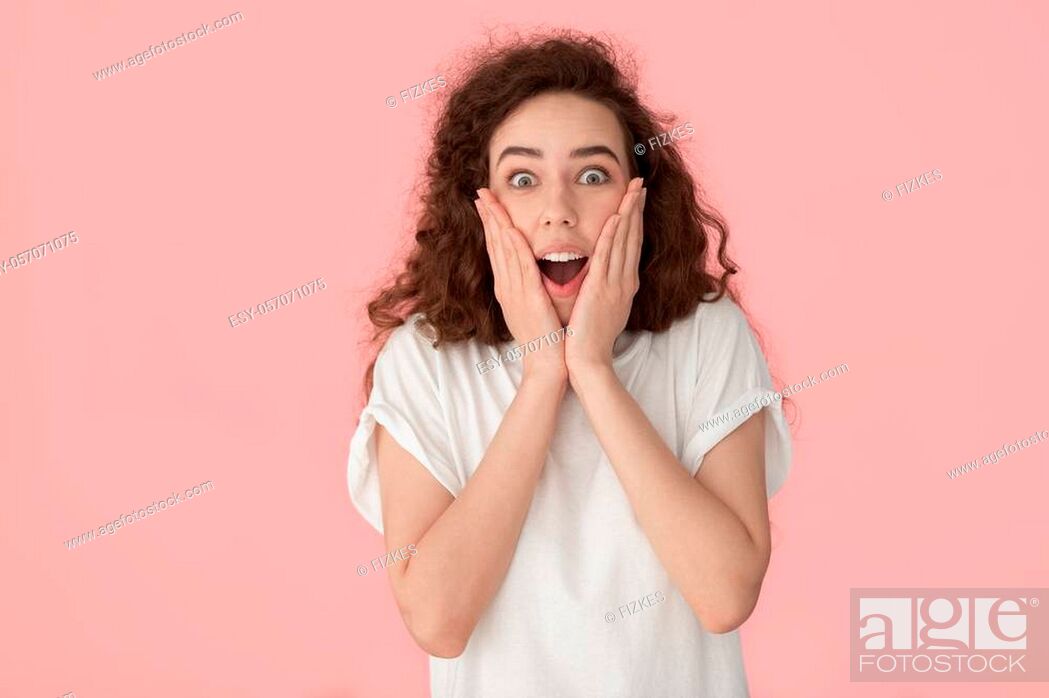 Stock Photo: Studio shot excited surprised amazed curly brown-haired woman open mouth feels astonishment touch face with hands look at camera isolated on pink background.