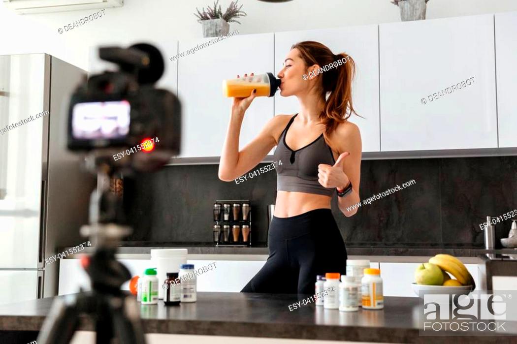 Stock Photo: Satisfied healthy young girl recording her video blog episode about healthy food additives while standing at the kitchen at home and showing thumbs up.