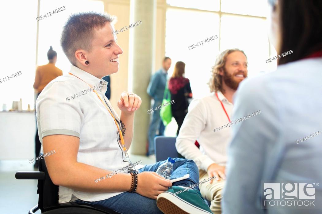 Stock Photo: Smiling woman in wheelchair talking to colleagues at conference.