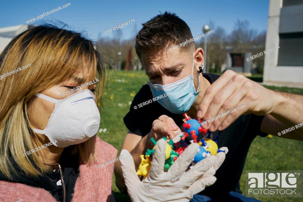 Stock Photo: Asian woman with a protective mask with virus models on her hands and a Caucasian guy points at them. The concept of Coronavirus.
