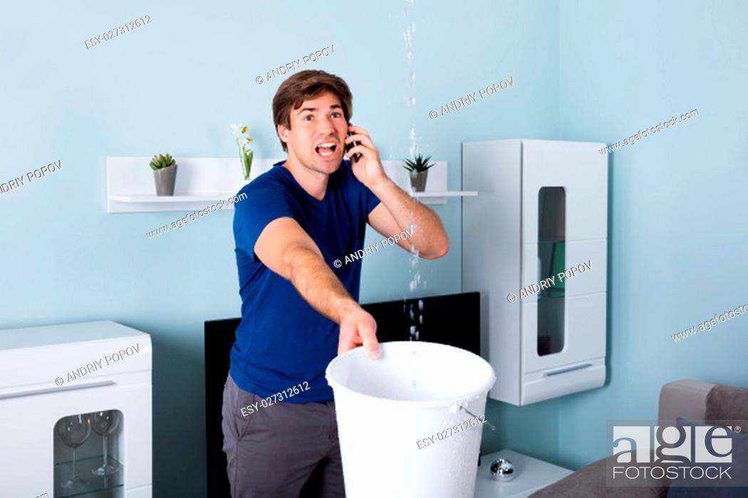 Photo de stock: Worried Man Calling Plumber While Leakage Water Falling Into Bucket At Home.