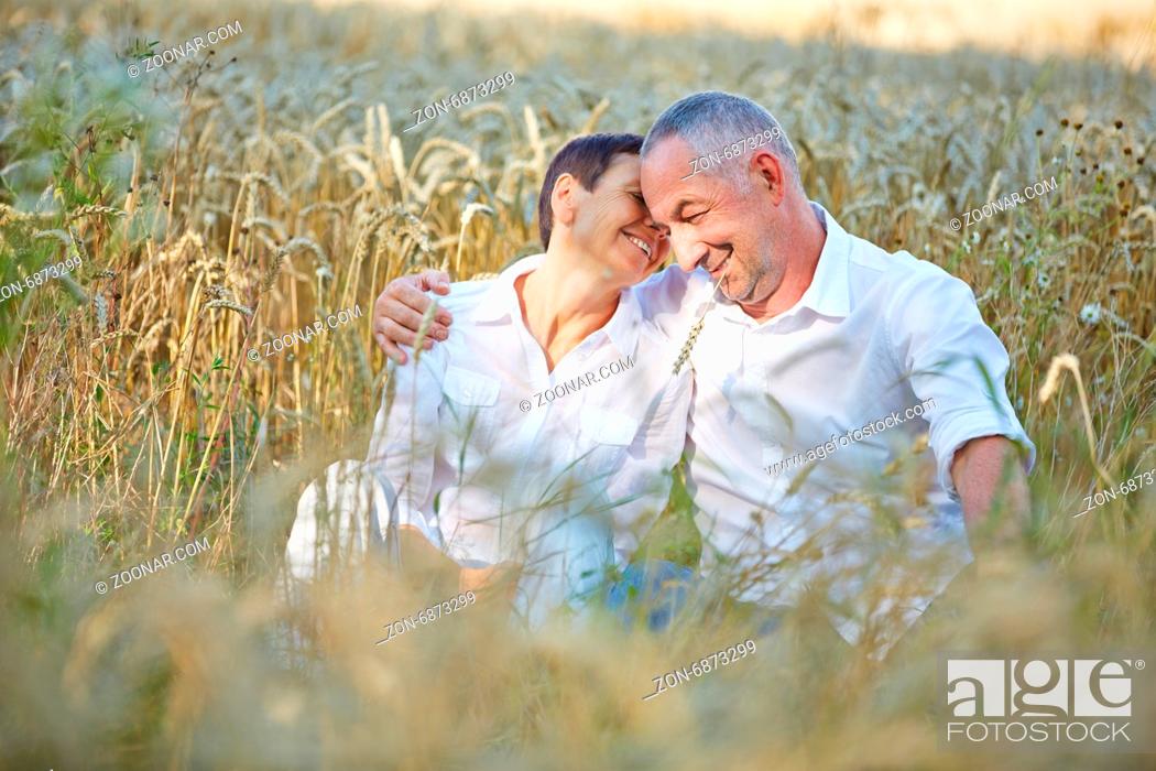 Stock Photo: Zufriedenes Paar Senioren im Urlaub sitzt im Sommer in einem Feld voller Weizen.