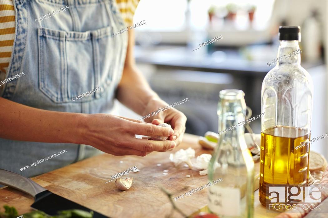 Stock Photo: Woman in kitchen preparing garlic for cooking on chopping board.