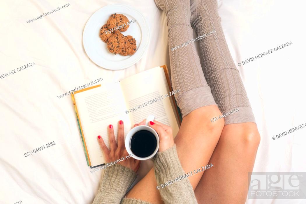 Photo de stock: Woman eating breakfast in bed while reading a book .