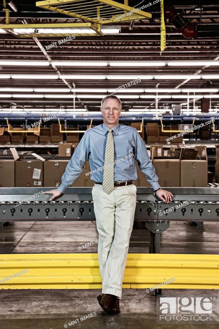 Stock Photo: Portrait of a male Caucasian executive in a dress shirt and tie next to a motorized conveyor system in a large distribution warehouse.