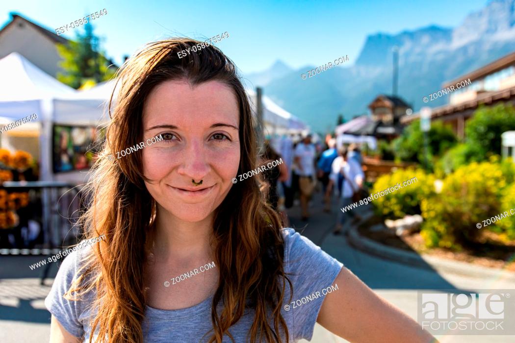 Stock Photo: Front portrait of a happy caucasian girl with brown hair and eyes, smiling against a blurred background during a local fair for artisans and traders.