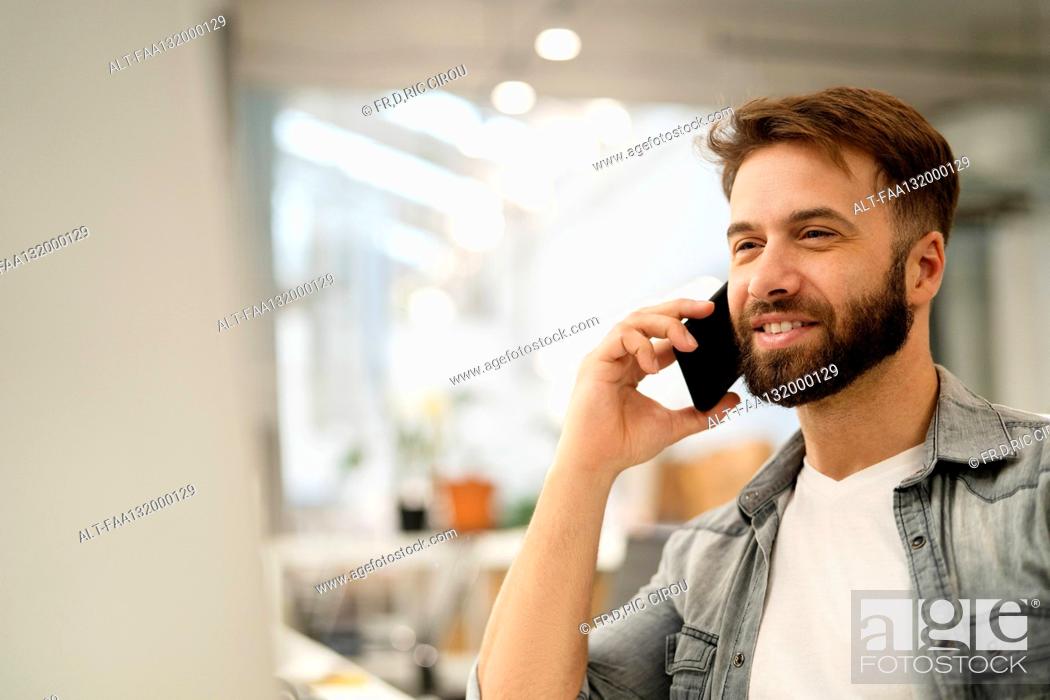 Photo de stock: Male system engineer listening to voice mail while using computer.