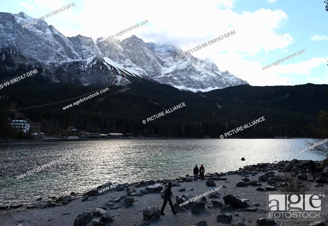 Stock Photo: 20 November 2022, Bavaria, Grainau: Strollers walk along the shore of the Eibsee, in the background you can see the Wetterstein mountains.
