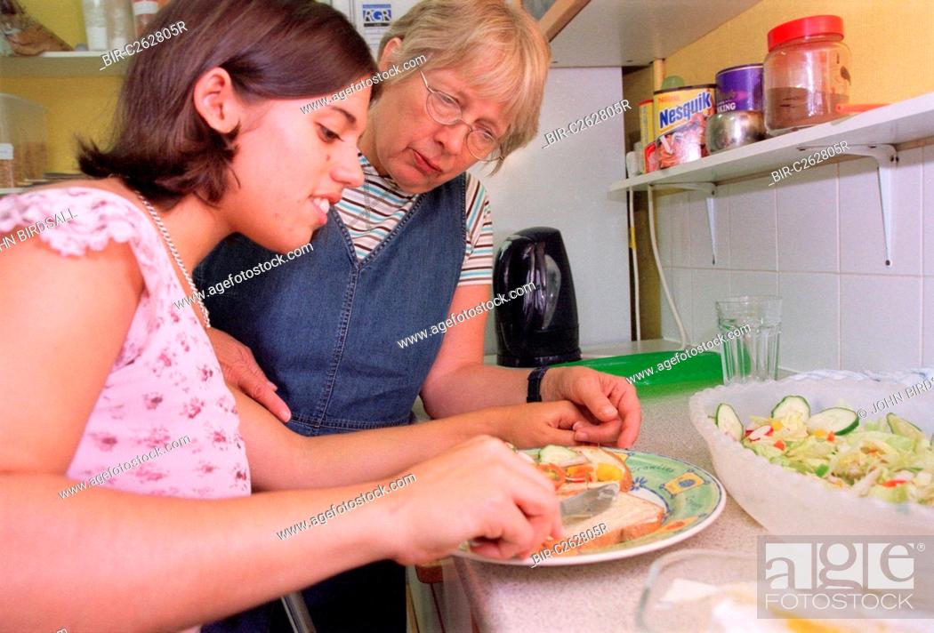 Stock Photo: Carer assisting teenage girl with physical disability to prepare a sandwich in kitchen of residential respite care home,.