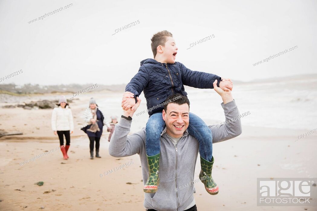 Imagen: Happy father carrying son with Down Syndrome on shoulders on beach.