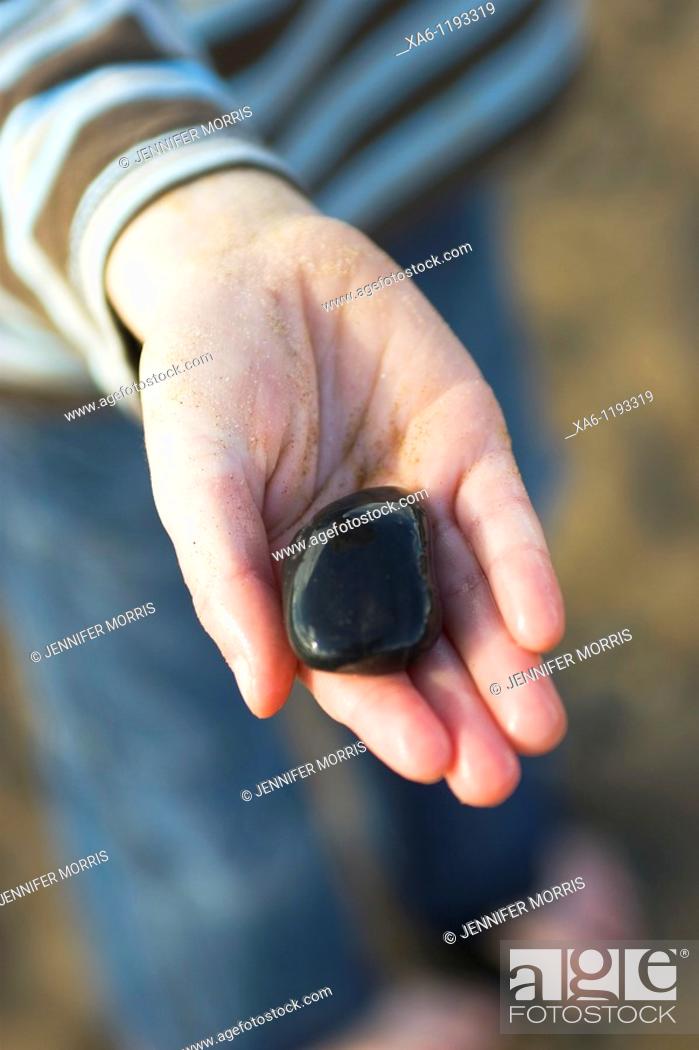 Stock Photo: A young boy's sandy hand holds a shiny wet black stone.