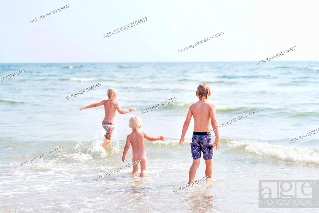 Photo de stock: Three boys walking in sea on beach.