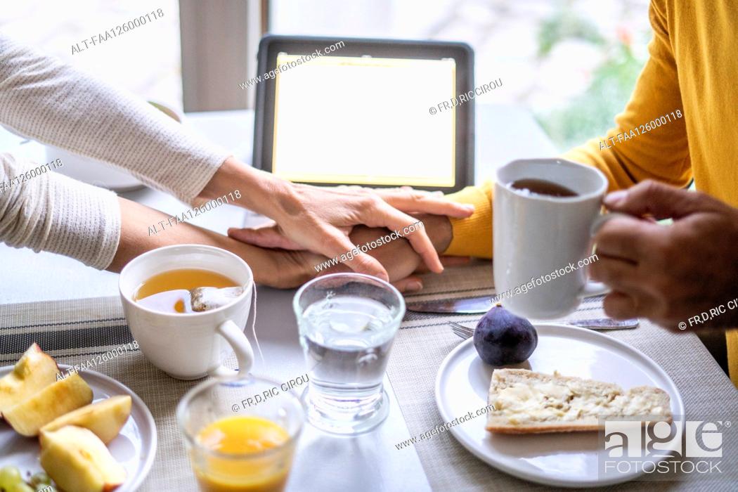 Photo de stock: Mature couple holding hands while having breakfast at table.