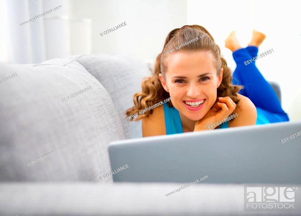 Stock Photo: Young woman laying on sofa and using laptop.