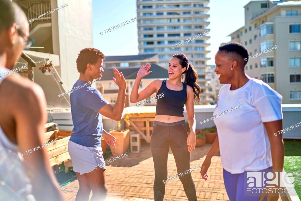 Imagen: Young friends exercising and high fiving on sunny urban rooftop.